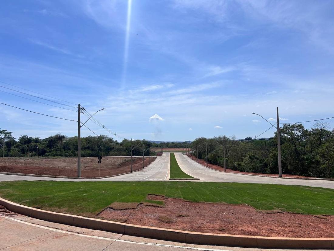Avenida de loteamento recém-pavimentada, com canteiro central gramado e iluminação instalada